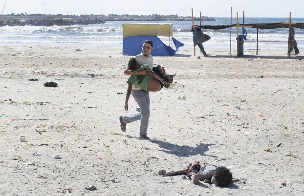 **EDS.: PLEASE NOTE GRAPHIC CONTENT** A man carries a child as another lies dead after two explosions on a beach in Gaza, July 16, 2014. At least four children playing on a Gaza beach were killed Wednesday, according to witnesses, after reportedly being attacked by an Israeli gunboat. (Tyler Hicks/The New York Times)